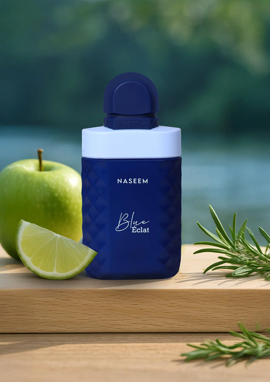 Naseem Blue Éclat 100ml parfum bottle on a wooden board, styled with a green apple, lime slice, and fresh rosemary sprigs